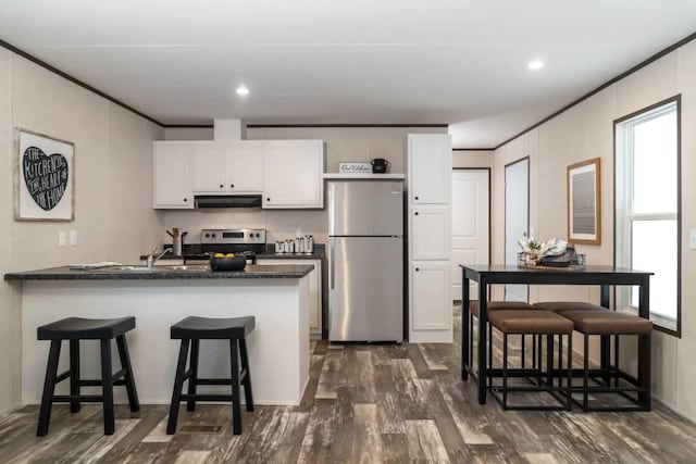 kitchen featuring appliances with stainless steel finishes, a kitchen breakfast bar, dark wood-type flooring, crown molding, and white cabinets