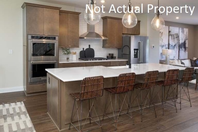 kitchen with a kitchen bar, appliances with stainless steel finishes, decorative light fixtures, and wall chimney range hood