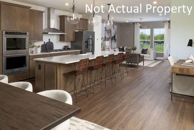 kitchen with decorative backsplash, appliances with stainless steel finishes, wall chimney exhaust hood, dark hardwood / wood-style floors, and an island with sink