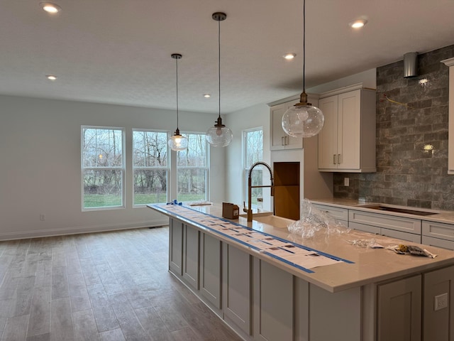 kitchen featuring gray cabinetry, light stone counters, stovetop, light hardwood / wood-style floors, and a kitchen island with sink