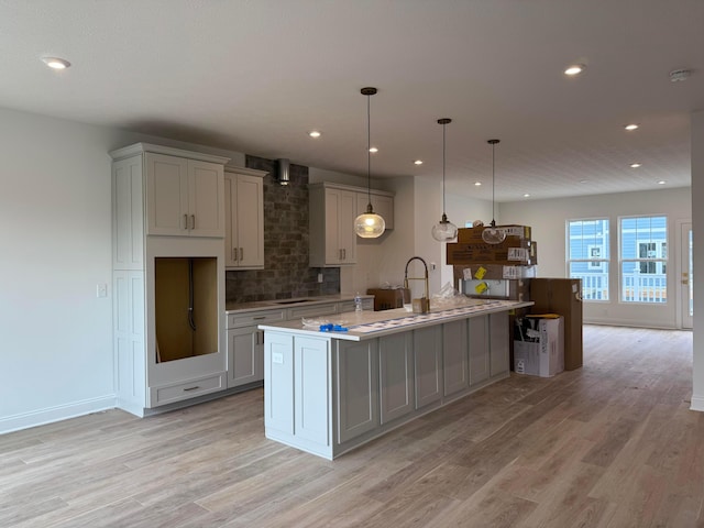 kitchen featuring gray cabinets, a kitchen island with sink, pendant lighting, and light hardwood / wood-style floors