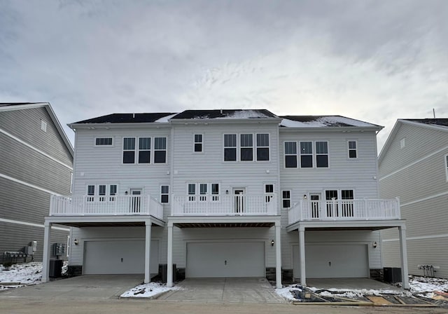 snow covered house with a balcony, central AC unit, and a garage