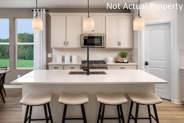 kitchen with white cabinetry, hanging light fixtures, light hardwood / wood-style flooring, a center island with sink, and appliances with stainless steel finishes