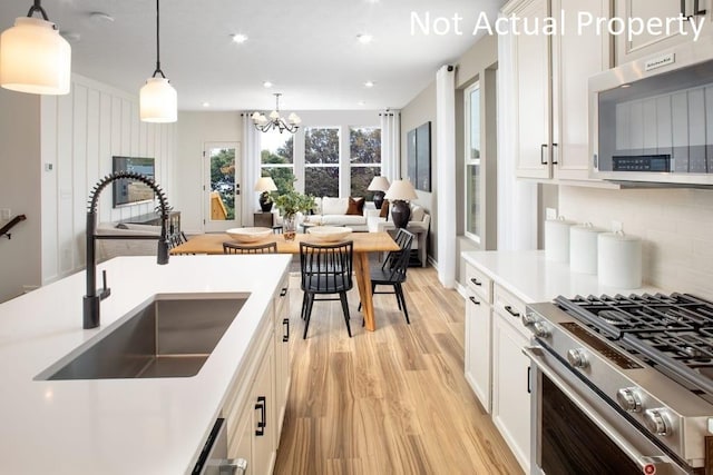 kitchen with an inviting chandelier, sink, hanging light fixtures, white cabinetry, and stainless steel appliances