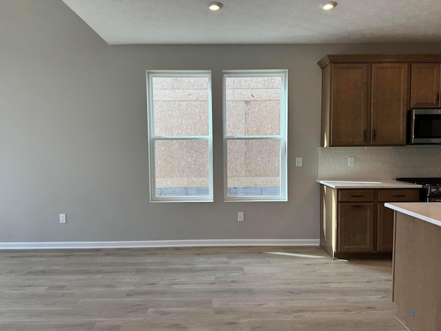 kitchen with tasteful backsplash, baseboards, stainless steel microwave, light countertops, and light wood-type flooring