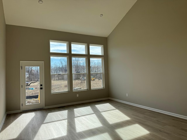 unfurnished room with baseboards, high vaulted ceiling, wood finished floors, and a healthy amount of sunlight