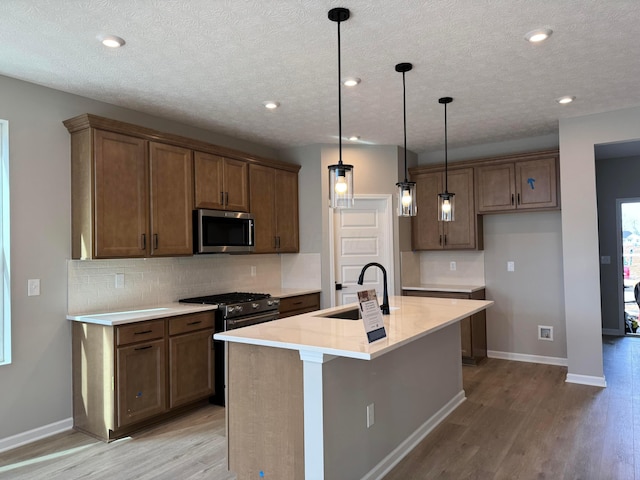 kitchen featuring light wood-style flooring, a sink, baseboards, appliances with stainless steel finishes, and backsplash