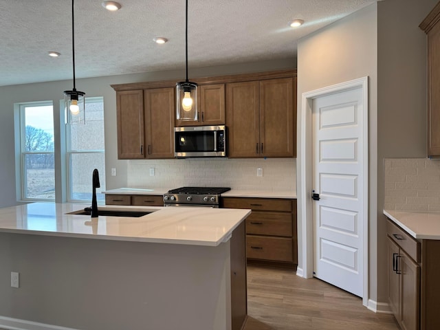 kitchen featuring decorative light fixtures, light countertops, appliances with stainless steel finishes, light wood-style floors, and a sink