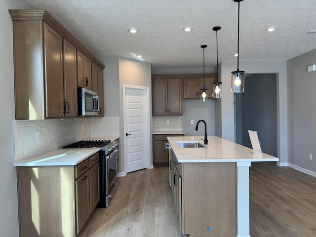 kitchen featuring light wood finished floors, hanging light fixtures, backsplash, appliances with stainless steel finishes, and a sink