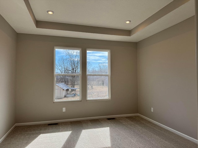 spare room with carpet, recessed lighting, a raised ceiling, visible vents, and baseboards