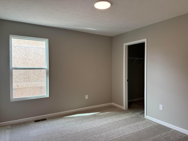 carpeted empty room with a textured ceiling, visible vents, and baseboards