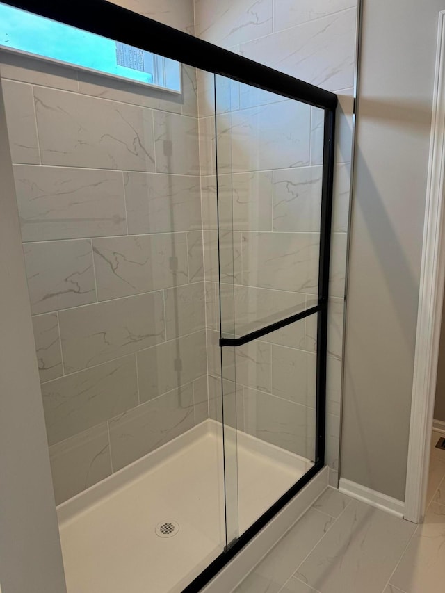 bathroom with marble finish floor, a shower stall, and baseboards