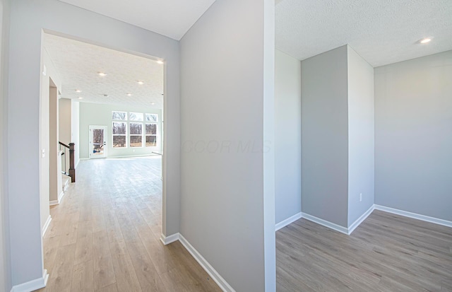 corridor with stairs, wood finished floors, baseboards, and a textured ceiling