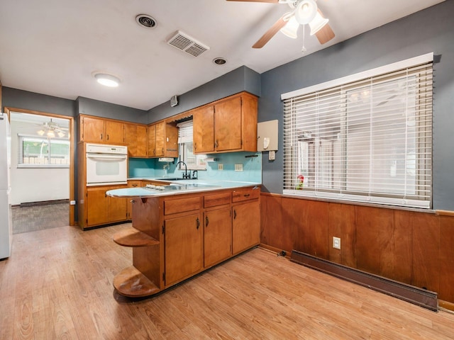 kitchen with white appliances, light hardwood / wood-style flooring, ceiling fan, a baseboard radiator, and kitchen peninsula