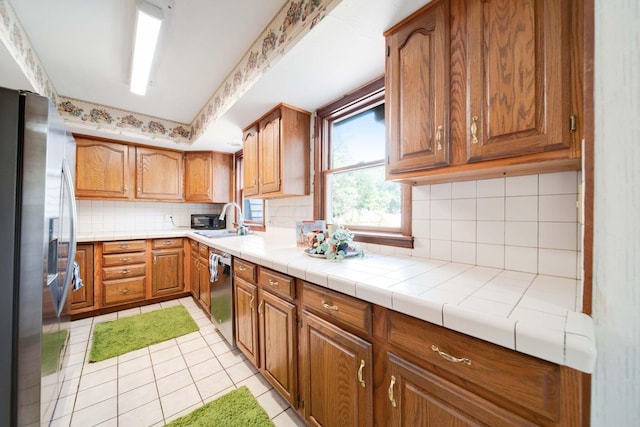 kitchen featuring appliances with stainless steel finishes, tasteful backsplash, sink, light tile patterned floors, and tile countertops