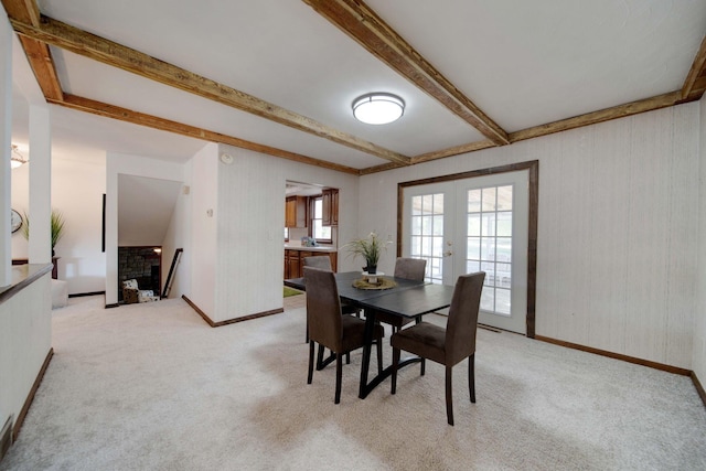 carpeted dining space with beamed ceiling, french doors, and a fireplace