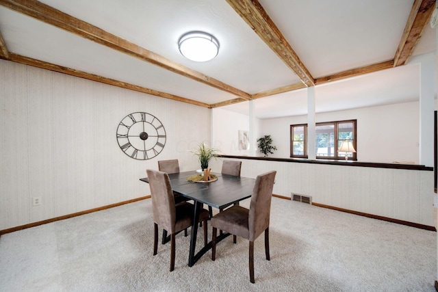 dining space with beamed ceiling and light carpet