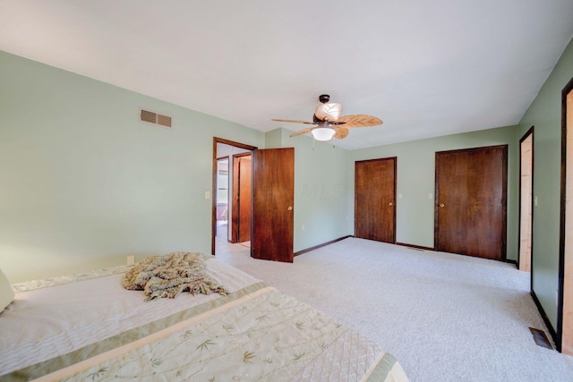 unfurnished bedroom featuring multiple closets, ceiling fan, and light colored carpet