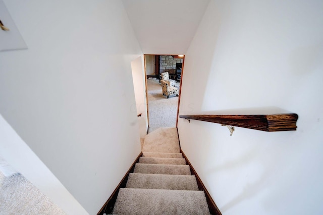 staircase featuring carpet flooring and a stone fireplace