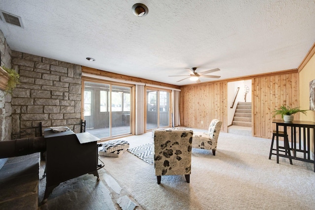 carpeted living room with wood walls, ceiling fan, and a textured ceiling