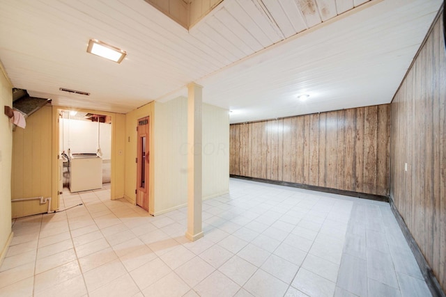 basement with light tile patterned flooring, washer / clothes dryer, and wooden walls