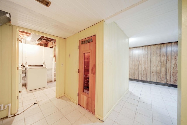 corridor with wood walls, light tile patterned floors, and washer / dryer