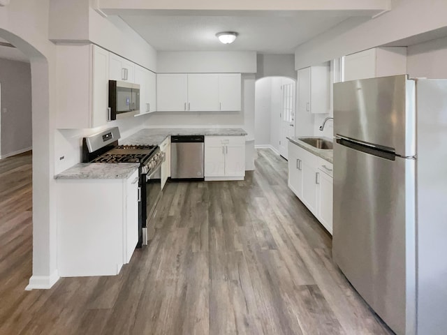 kitchen featuring light stone countertops, stainless steel appliances, sink, hardwood / wood-style floors, and white cabinetry