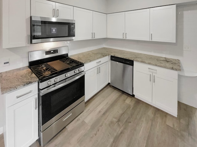 kitchen featuring white cabinets, stainless steel appliances, light stone countertops, and light hardwood / wood-style floors