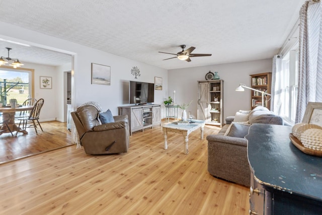 living room featuring ceiling fan, light hardwood / wood-style flooring, and a textured ceiling