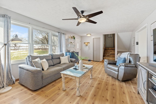 living room with ceiling fan, a textured ceiling, and light wood-type flooring