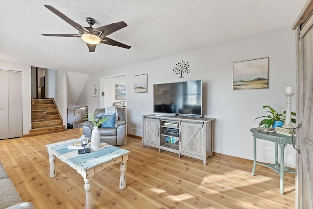 living room featuring ceiling fan, light hardwood / wood-style flooring, a barn door, and a textured ceiling