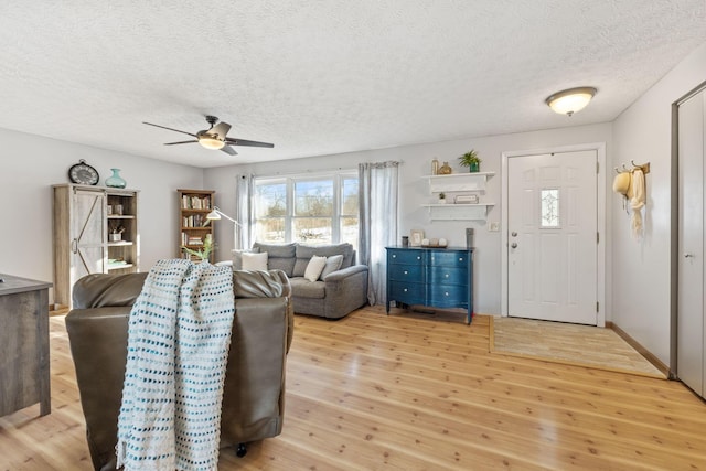 living room with ceiling fan, a textured ceiling, and light wood-type flooring