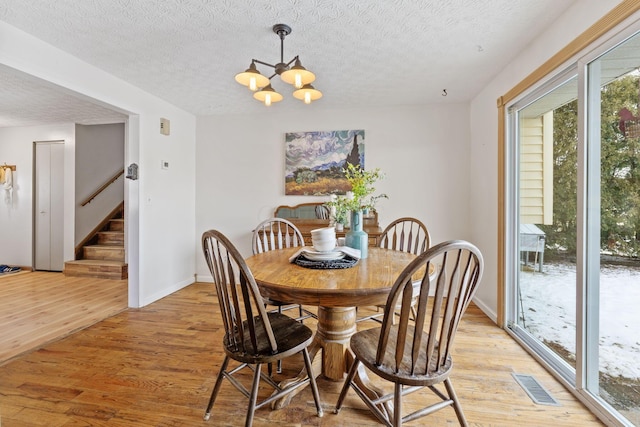 dining space with a notable chandelier, a textured ceiling, and light wood-type flooring