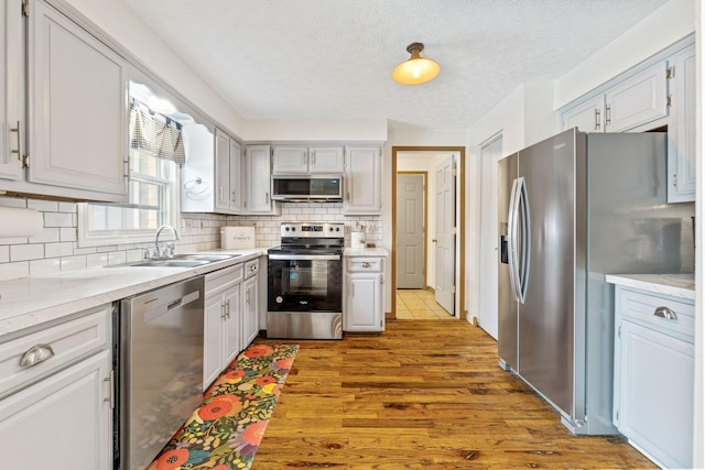 kitchen with sink, tasteful backsplash, light hardwood / wood-style flooring, a textured ceiling, and stainless steel appliances