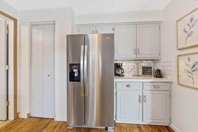 kitchen with tasteful backsplash, stainless steel fridge with ice dispenser, light hardwood / wood-style flooring, and a textured ceiling