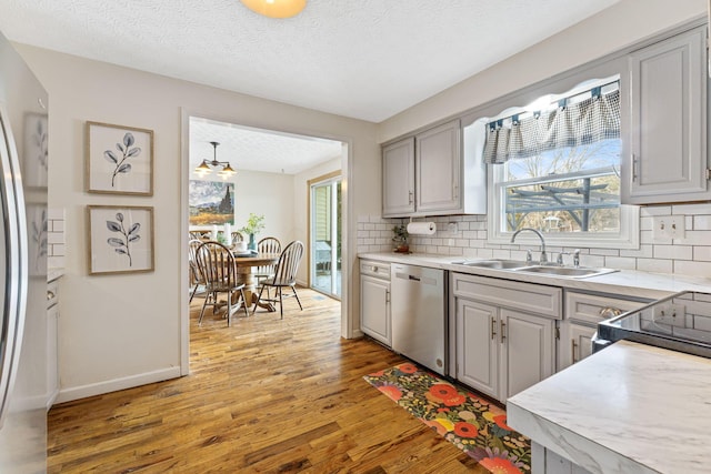 kitchen with gray cabinets, appliances with stainless steel finishes, sink, backsplash, and light hardwood / wood-style flooring