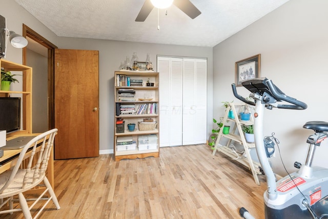 workout area with ceiling fan, light hardwood / wood-style flooring, and a textured ceiling