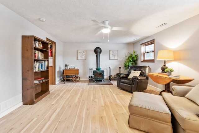 sitting room featuring ceiling fan, light hardwood / wood-style flooring, a textured ceiling, and a wood stove