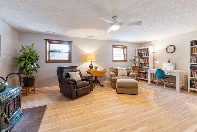 sitting room with ceiling fan, light wood-type flooring, a textured ceiling, and a wood stove