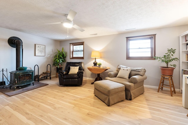 living area with ceiling fan, a textured ceiling, light hardwood / wood-style flooring, and a wood stove