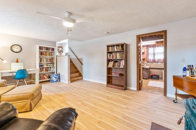 living room featuring ceiling fan, light hardwood / wood-style floors, and a textured ceiling