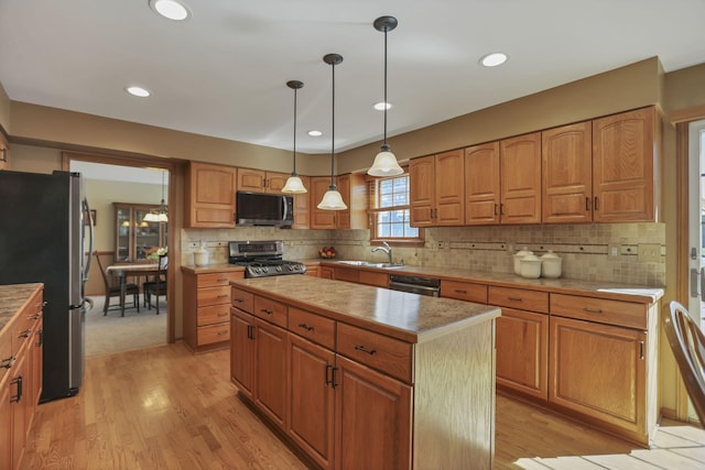 kitchen with stainless steel appliances, sink, decorative light fixtures, light hardwood / wood-style flooring, and a kitchen island