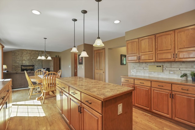 kitchen featuring backsplash, pendant lighting, light hardwood / wood-style floors, a kitchen island, and a stone fireplace