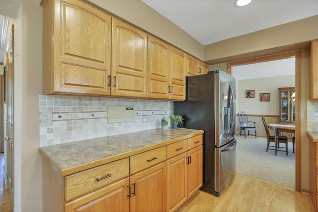 kitchen with stainless steel refrigerator with ice dispenser, light wood-type flooring, and backsplash