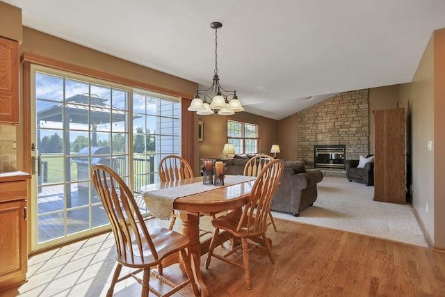 dining space with a notable chandelier, light hardwood / wood-style flooring, a fireplace, and vaulted ceiling