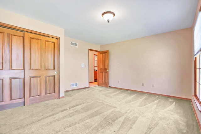 unfurnished bedroom with light colored carpet and a closet