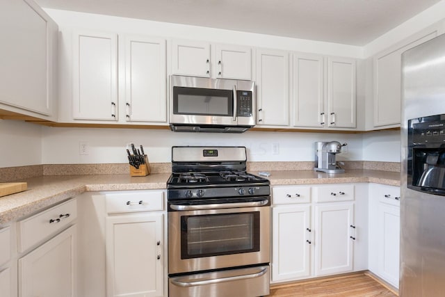 kitchen with stainless steel appliances, white cabinetry, and light hardwood / wood-style flooring