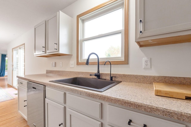 kitchen with stainless steel dishwasher, a wealth of natural light, sink, and white cabinets