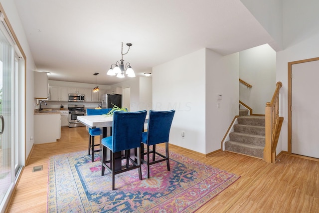 dining area featuring an inviting chandelier, sink, and light hardwood / wood-style floors