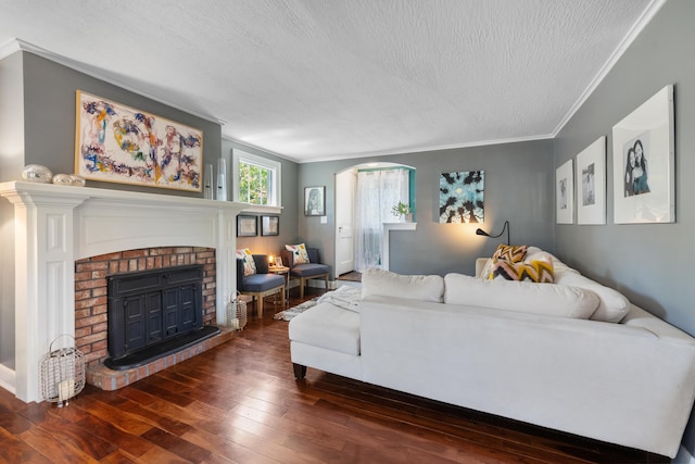 living room featuring dark hardwood / wood-style flooring, ornamental molding, a textured ceiling, and a brick fireplace